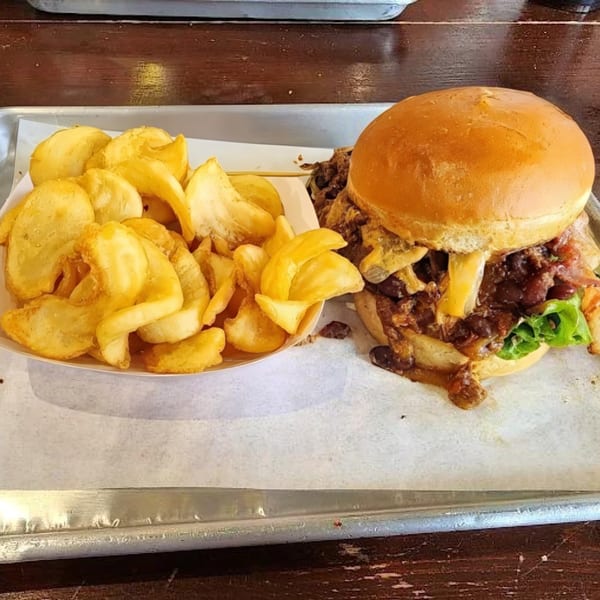 A Bunz Handcrafted Burger with melted cheese, caramelized onions, and lettuce, served with golden potato wedges.