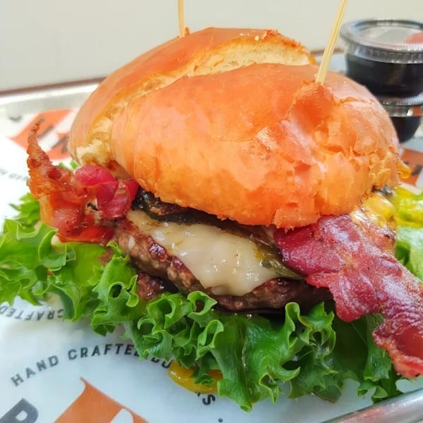 A Bunz Handcrafted Burger with melted cheese, bacon, lettuce, and red relish on a brioche bun.