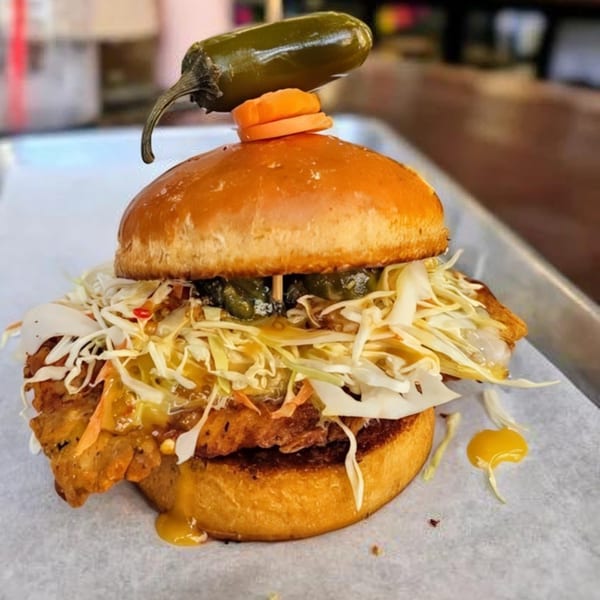 A Bunz Handcrafted Burger with crispy fried chicken, coleslaw, and jalapeños on a brioche bun.
