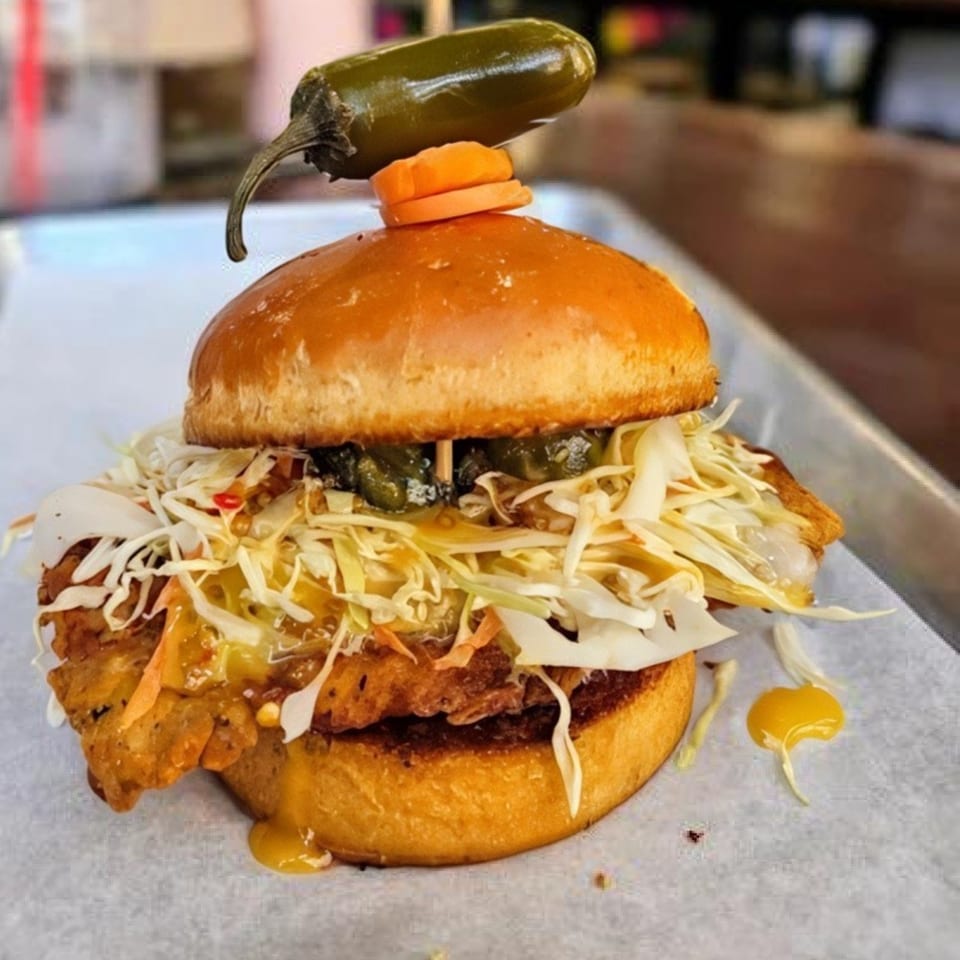 A Bunz Handcrafted Burger with crispy fried chicken, coleslaw, and jalapeños on a brioche bun.