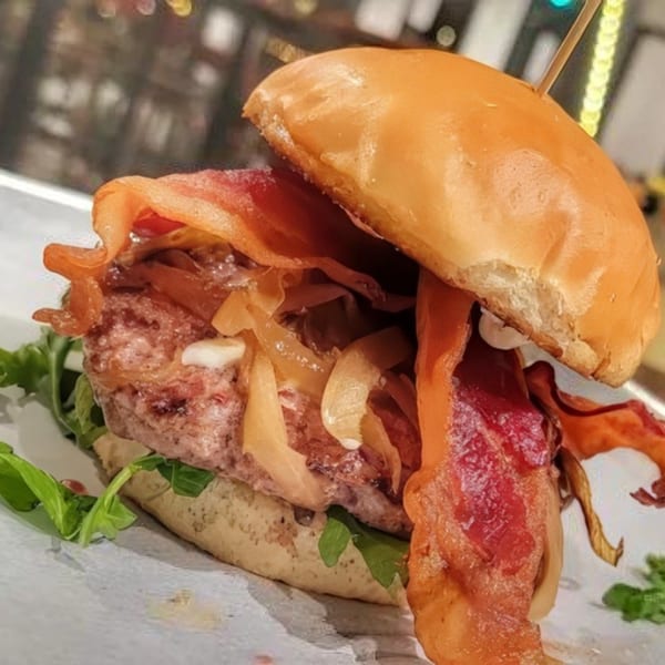 Close-up of a Bunz Handcrafted Burger with bacon, caramelized onions, and arugula on a bun.