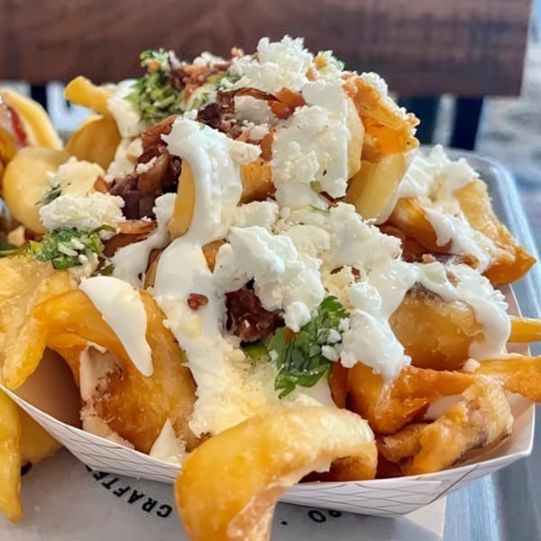 Close-up of Bunz Handcrafted Burgers' loaded fries with white sauce, crumbled cheese, and bacon bits.